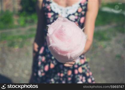 A young woman wearing a dress is standing outside with a candyfloss on a sunny summer day