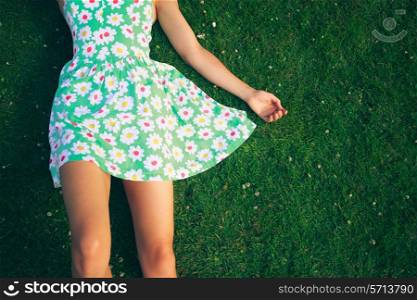 A young woman wearing a flowery dress is lying on the grass in summer