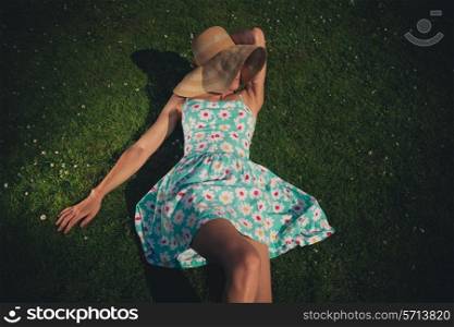 A young woman wearing a hat and a summer dress is relaxing on the grass