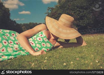 A young woman wearing a hat and a summer dress is relaxing on the grass