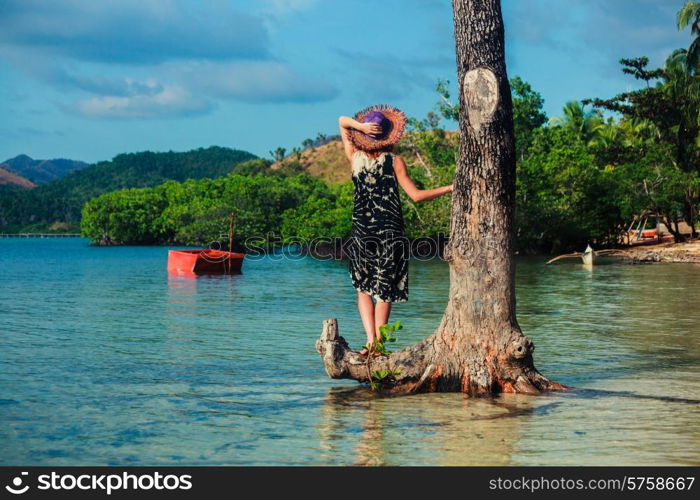 A young woman wearing a hat by a tree on a tropical beach
