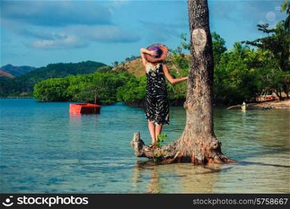 A young woman wearing a hat by a tree on a tropical beach
