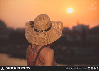 A young woman wearing a hat is admiring the sunset in the city