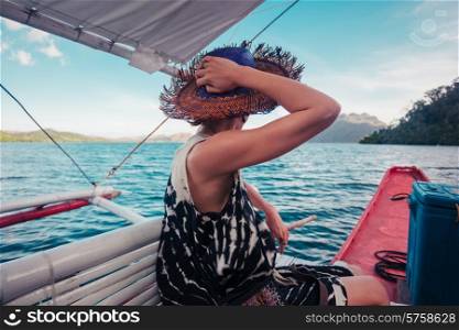 A young woman wearing a hat is on a boat in the tropics