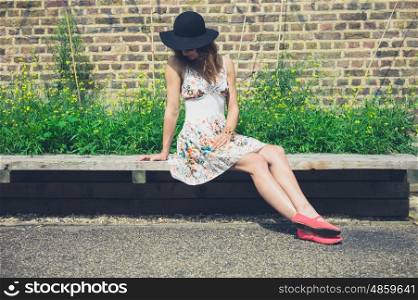 A young woman wearing a hat is sitting on a bench and relaxing outside in the summer
