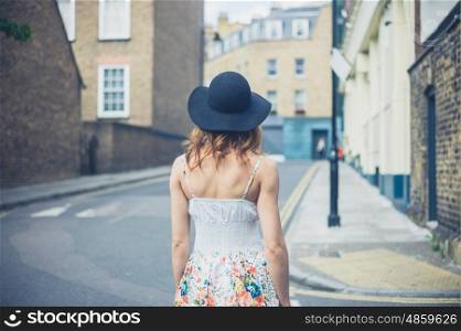 A young woman wearing a hat is walking in the street