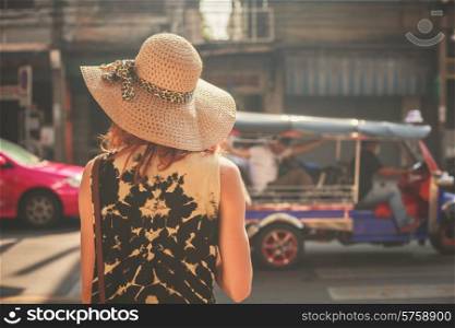 A young woman wearing a hat is walking in the streets of an asian country
