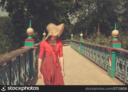 A young woman wearing a red dress is standing on a bridge in a park