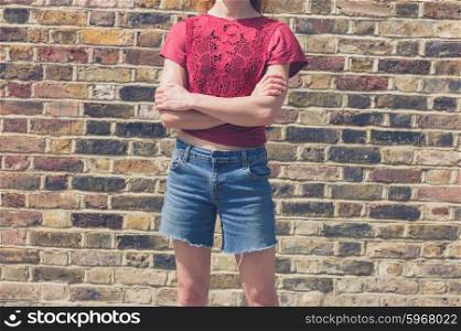 A young woman wearing a red top is standing in the street by a brick wall