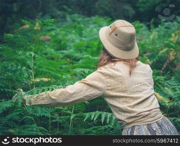 A young woman wearing a safari hat is exploring a forest with lots of green ferns