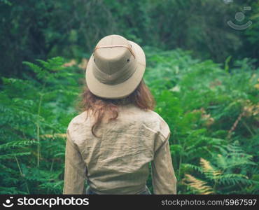 A young woman wearing a safari hat is exploring a forest with lots of green ferns