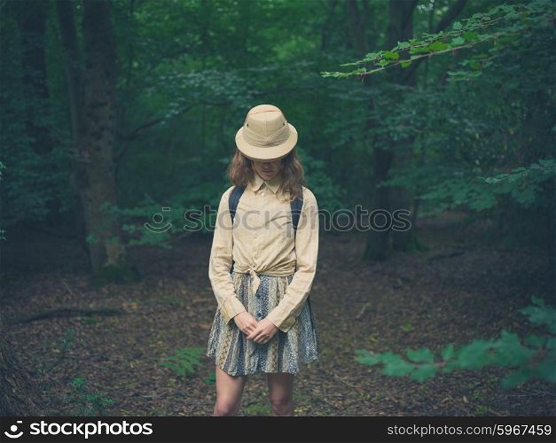 A young woman wearing a safari hat is standing in the forest