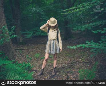 A young woman wearing a safari hat is standing in the forest
