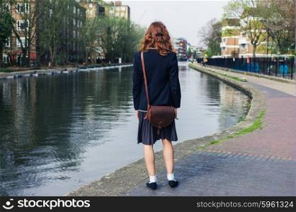A young woman wearing a skirt and a jacket is standing by a canal in the spring