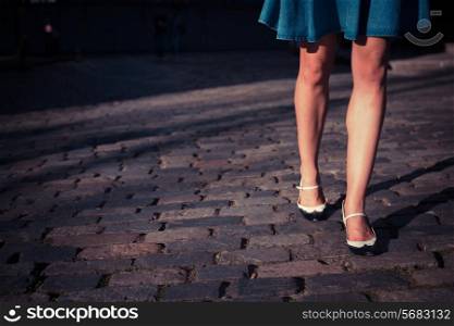 A young woman wearing a skirt and retro shoes is walking on a cobbled street at sunset