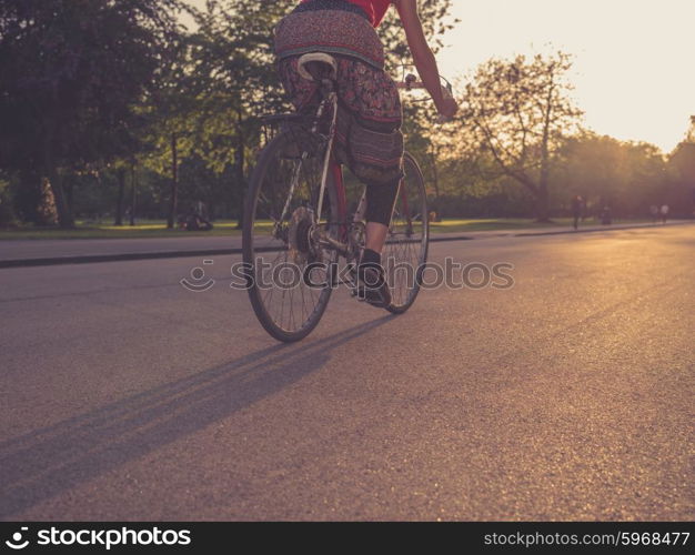 A young woman wearing a skirt is riding a bicycle in the park at sunset