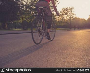 A young woman wearing a skirt is riding a bicycle in the park at sunset