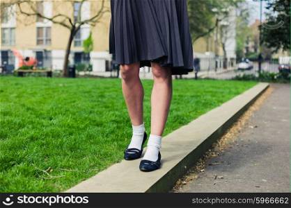 A young woman wearing a skirt is walking in a park by the green grass