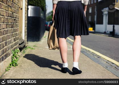 A young woman wearing a skirt is walking in the street on a sunny day