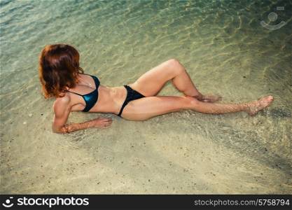 A young woman wearing a swimsuit is lying in the water on a tropical beach