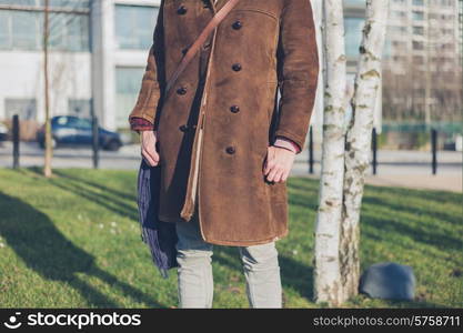 A young woman wearing a warm coat is standing by some birch trees in a park