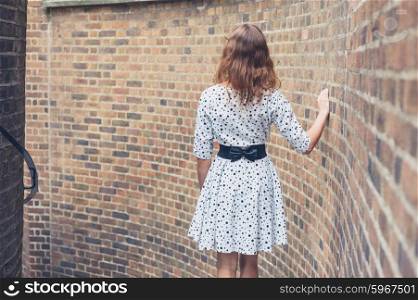 A young woman wearing a white summer dress is standing on some stairs outside by a brick wall
