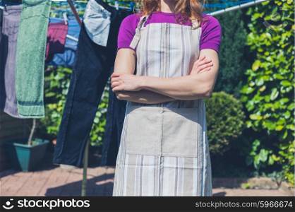 A young woman wearing an apron is standing by her laundry drying on a clothes line in the garden