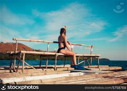 A young woman wearing flippers and snorkeling mask is sitting on a raft in a tropical location