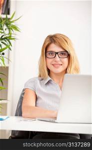 A young woman wearing glasses in front of a laptop sitting in the office