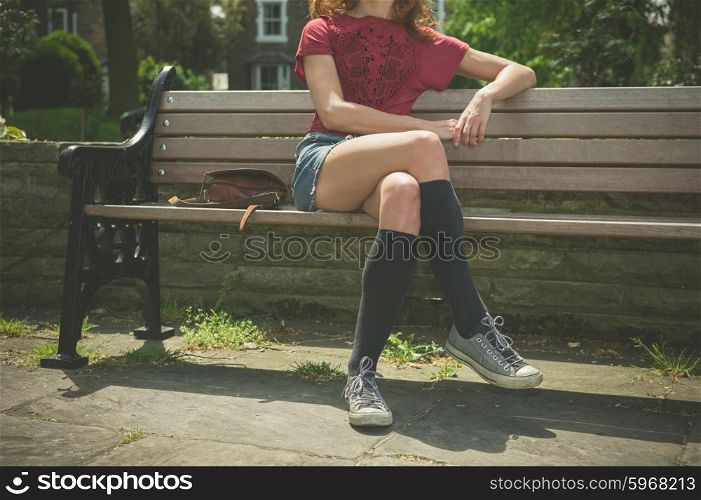 A young woman wearing knee high socks is sitting on a park bench