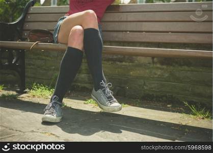 A young woman wearing knee high socks is sitting on a park bench