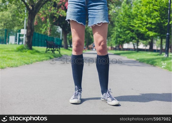 A young woman wearing knee high socks is standing in a park on a summer day