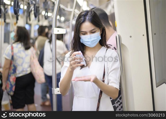 A young woman wearing protective mask in subway is using alcohol to wash hands, travel under Covid-19 pandemic, safety travels, social distancing protocol, New normal travel concept