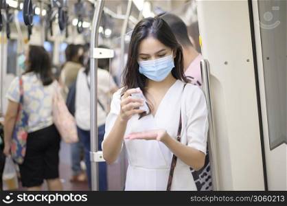 A young woman wearing protective mask in subway is using alcohol to wash hands, travel under Covid-19 pandemic, safety travels, social distancing protocol, New normal travel concept