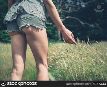 A young woman wearing short shorts is touching the grass as she is walking in a meadow in the forest