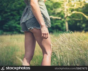 A young woman wearing shorts is standing in a meadow in the forest on a sunny summer day