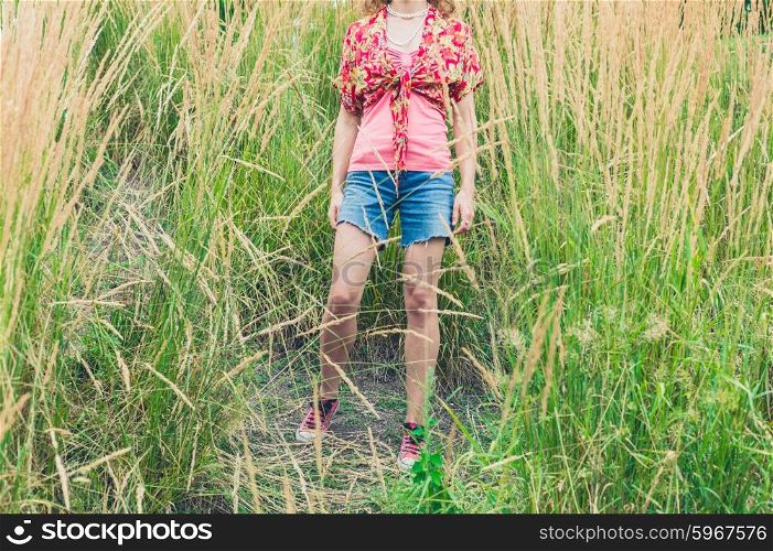 A young woman wearing shorts is standing outside in some tall grass