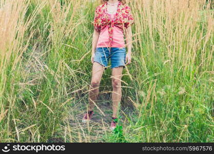 A young woman wearing shorts is standing outside in some tall grass