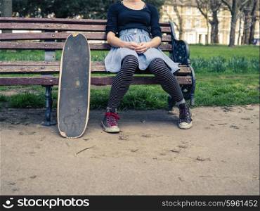 A young woman with a skateboard is sitting on a park bench