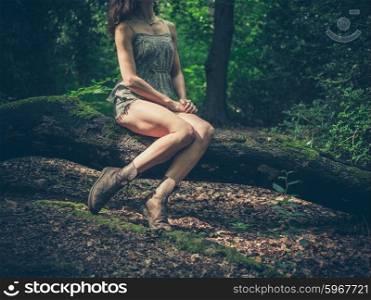 A young woman with bare legs is sitting on a log in the forest
