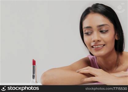 A young woman with clear,spotless skin looking at a lipstick kept beside.