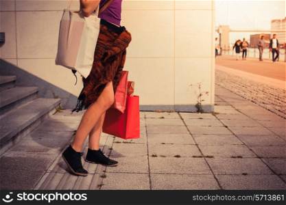 A young woman with shopping bags is standing by some stairs outside at sunset