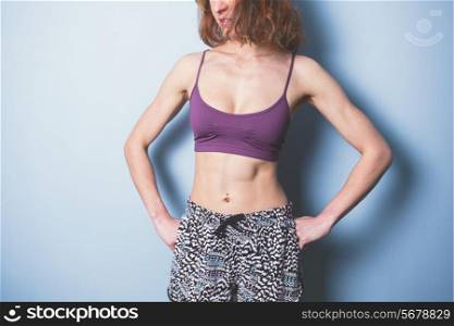A young woman with toned abs is wearing sports clothing and standing against a blue background