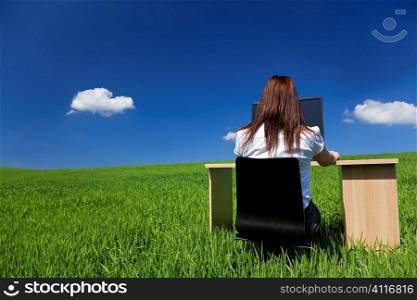 A young woman working on a desk in a green field