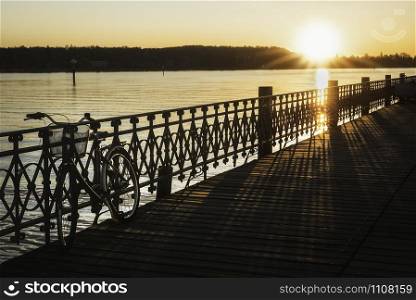 Abandoned bicycle on a wooden pier over lake Constance water at sunrise, in Konstanz, Germany. Deck over Bodensee lake at dawn. Sunny day at lake.