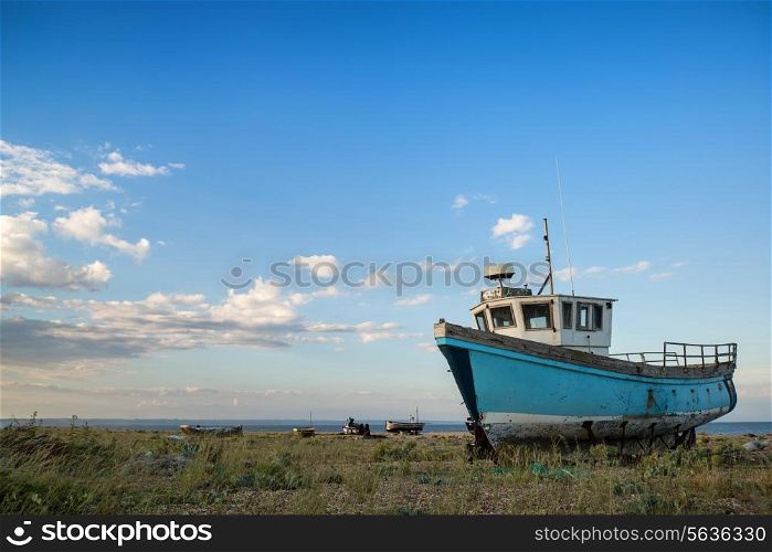 Abandoned fishing boat on shingle beach landscape at sunset