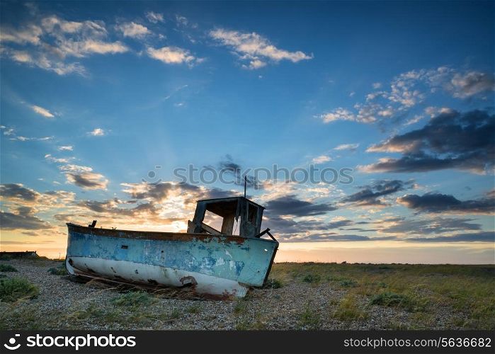 Abandoned fishing boat on shingle beach landscape at sunset