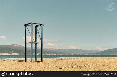 Abandoned lifeguard tower on a pebbly beach, Black Sea coast, empty beach on a sunny day in April. The sky is burnt out at noon, the sea bay in the background is the Caucasian mountains