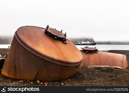 Abandoned norwegian whale hunter station rusty blubber tanks with cruise vessel in the bay , at Deception island, Antarctic8