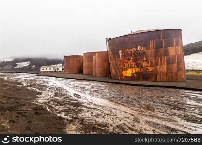 Abandoned norwegian whale hunter station rusty blubber tanks with muddy river in the foreground at Deception island, Antarctic